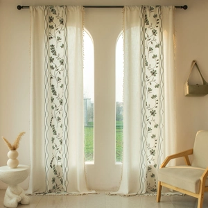 Detail of off-white linen curtains with green vine embroidery and tassel ball fringe
