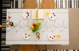 Close-up of rectangular beige linen tablecloth with brown leaf embroidery and tassels