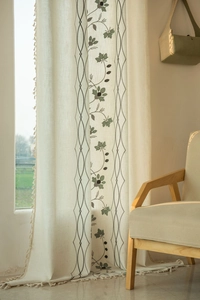 Close-up of semi-sheer beige cotton linen curtain with green leaf embroidery and tassels