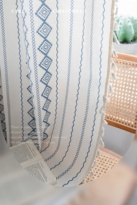 Detail of blue geometric patterns and delicate white tassels on cotton linen curtains