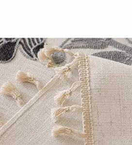 Détail macro de nappe en coton lin beige avec broderie de feuilles et pompons