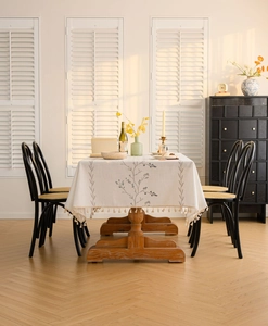 Detail of cream rectangular tablecloth with blue floral embroidery and fringe tassels