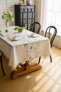 Close-up of blue floral embroidery and cotton fringe details on a beige linen tablecloth
