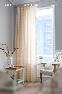 Detail of bohemian cream curtain with orange diamond prints and white fringe tassels