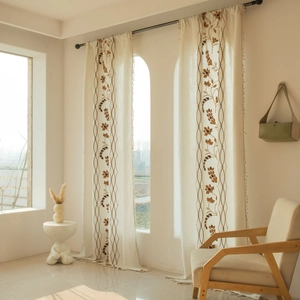 Detail of cream floral embroidery on linen-textured curtains with delicate fringe trim