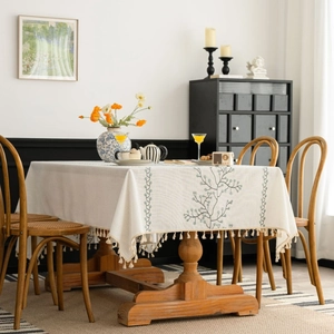 White linen tablecloth with green floral embroidery and beige fringe on a wooden table