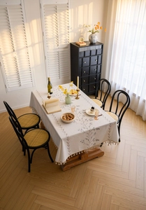 Close-up of rectangular cream tablecloth with blue floral embroidery and tassel fringe