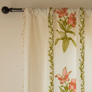 Dettaglio di tende beige ricamate con motivi floreali e nappe decorative sui bordi