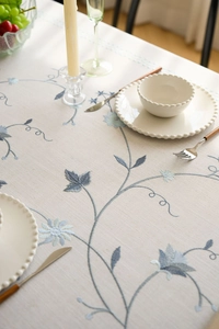 Close-up of floral embroidery on beige cotton linen tablecloth with tassel detail