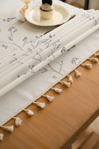 Detail of cream table runner featuring blue floral embroidery and fringe tassel edges