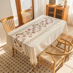 Close-up of floral embroidery and fringe tassels on a cream rectangle tablecloth