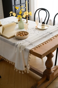 Close-up of lilac floral embroidery and beige tassels on a cotton linen tablecloth