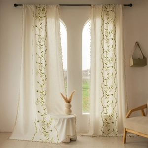 Close-up of green vine embroidery and beige tassel fringe on rustic linen curtains