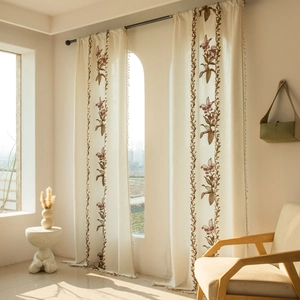 Dettaglio della tenda in lino crema con ricamo floreale e bordi decorativi con nappe