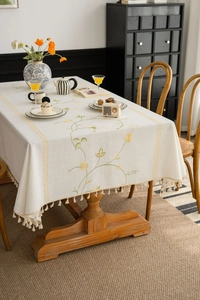 Detail of floral embroidery and fringe on a cream linen tablecloth in a vintage setting
