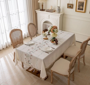 Close-up of floral embroidery and handmade fringe details on a cream rectangular tablecloth