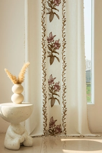 Dettaglio della tenda beige con ricamo floreale viola e bordi decorativi con nappe