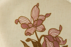 Dettaglio in primo piano di tessuto di lino beige con ricami floreali marroni e viola