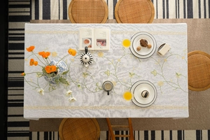 Detailed embroidery of yellow daisies and green vines on a cotton linen tablecloth