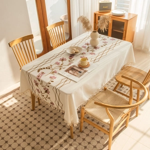 Close-up of floral embroidery and fringe tassels on a cream linen rectangle tablecloth