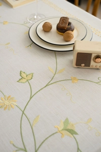 Detailed embroidery of yellow flowers and green vines on a beige cotton linen tablecloth