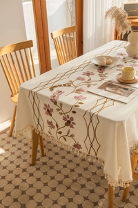 Close-up of pink flower embroidery and handmade tassels on beige linen tablecloth