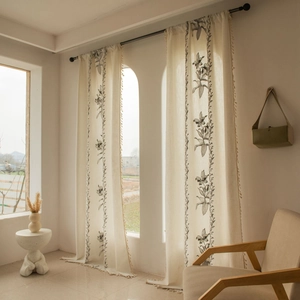 Dettaglio di tende ricamate beige con stampe floreali nere e piccole decorazioni con nappe