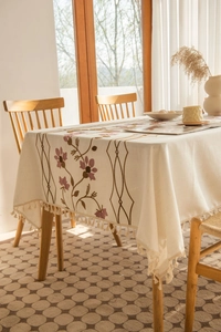 Close-up of beige tablecloth with purple floral embroidery and tassel fringe edges
