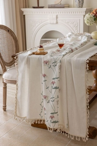 Close-up of elegant floral embroidery and tassel fringe on beige linen tablecloth