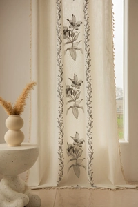 Dettaglio tenda in lino beige con stampe floreali e bordi decorati con frange a nappa