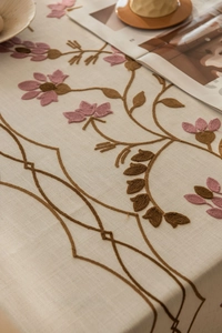 Close-up of floral embroidery on off-white linen tablecloth with rustic decor