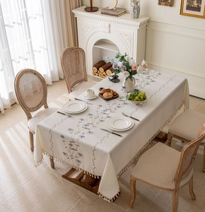 Close-up of cream rectangular tablecloth with blue floral embroidery and tassel fringe