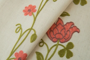 Close-up of beige fabric with orange floral embroidery and green leaves for curtains