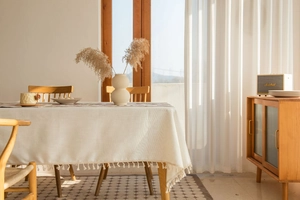 Close-up of beige linen tablecloth with elegant fringe tassels in a cozy home setting