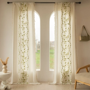 Detailed view of beige linen curtains with green vine embroidery and tassel edge