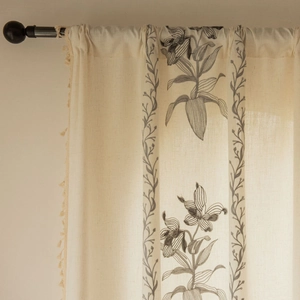 Primo piano di tende in lino beige con ricami floreali grigi e bordi decorativi con nappe
