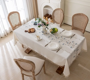Close-up of cream tablecloth with blue floral embroidery and fringe on wooden table
