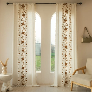 Detailed close-up of cream linen curtains with brown floral embroidery and tassel fringe
