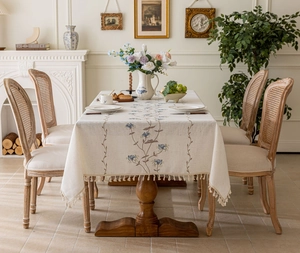 Detailed embroidery of blue flowers and beige tassels on cream linen tablecloth