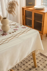 Detail of floral embroidery and elegant fringe edge on a thick cream linen tablecloth
