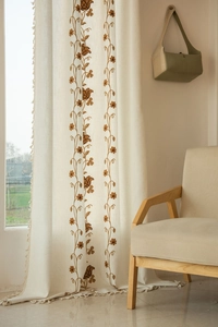 Close-up of beige cotton linen curtain with brown floral embroidery and tassel fringe