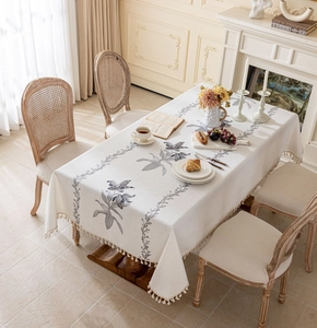 Détail de nappe beige vintage avec broderie florale bleue et bordures à pompons doux
