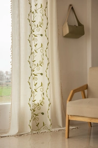 Close-up of olive green vine embroidery and tassel fringe on beige linen curtain