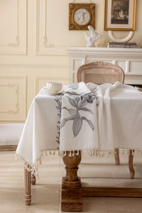 Détail de nappe rectangulaire beige avec broderie florale grise et bordure à franges