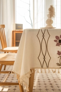 Detailed view of cream linen tablecloth with purple floral embroidery and tassels