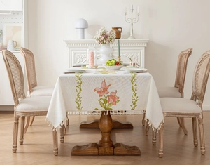 Détail de motifs floraux roses brodés et de pompons frangés sur nappe en lin beige