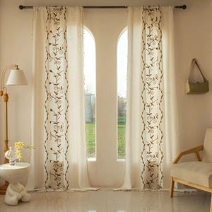 Detail of beige rustic curtains featuring vine embroidery and delicate tassel edges
