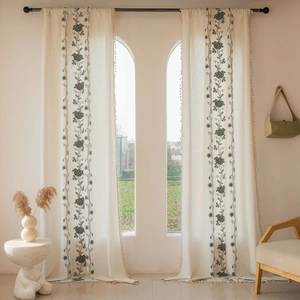 Detailed view of beige embroidered curtains with floral patterns and delicate tassels