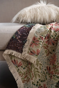 Detail of floral jacquard woven blanket with beige fringe tassels on a sofa