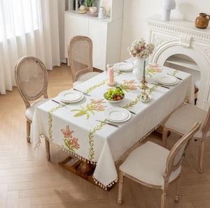 Détail de la nappe en lin beige avec broderie florale et finitions à franges de gland